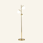 Slim brushed brass floor lamp with three opal white glass globes on angled branch arms, rising from a round metal base on cream backdrop.