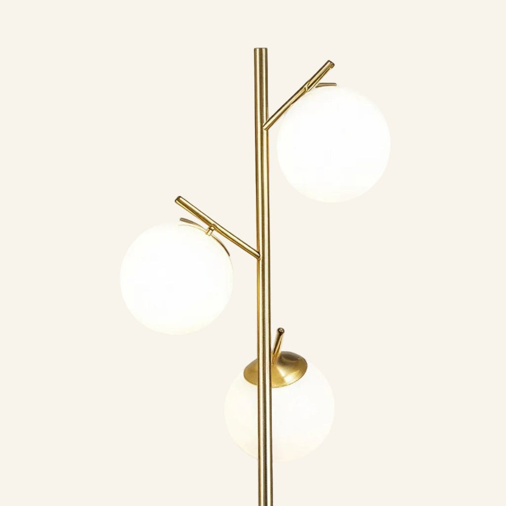 Close view of the brass stem and branching arms holding three frosted opal globe shades at staggered heights, showing smooth metal joinery.