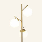 Close view of the brass stem and branching arms holding three frosted opal globe shades at staggered heights, showing smooth metal joinery.
