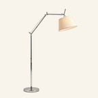 Polished aluminum swing arm floor lamp with tapered ivory fabric shade and round chrome base on cream studio background.
