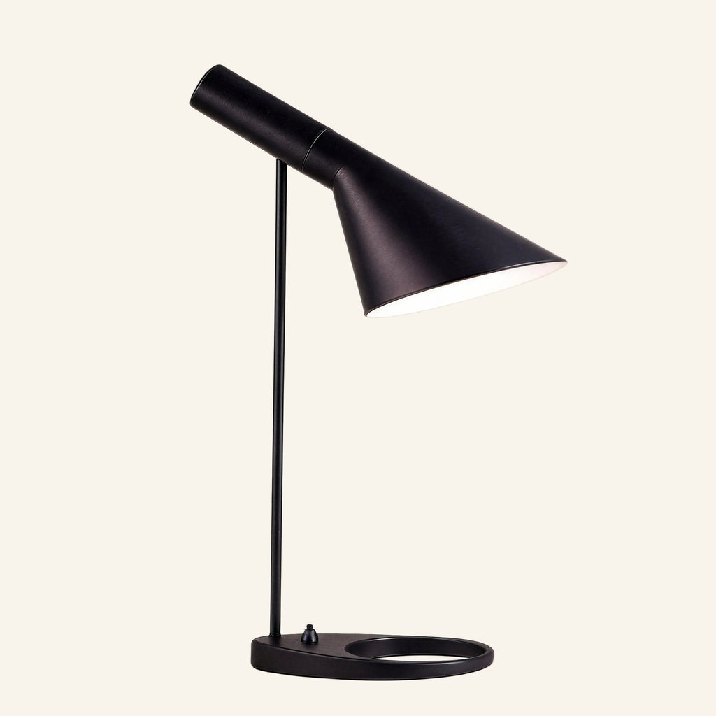 Matte black table lamp with tilting asymmetric cone shade, slim stem and oval ring base, Bauhaus-style metal task light on cream backdrop