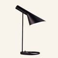 Matte black table lamp with tilting asymmetric cone shade, slim stem and oval ring base, Bauhaus-style metal task light on cream backdrop