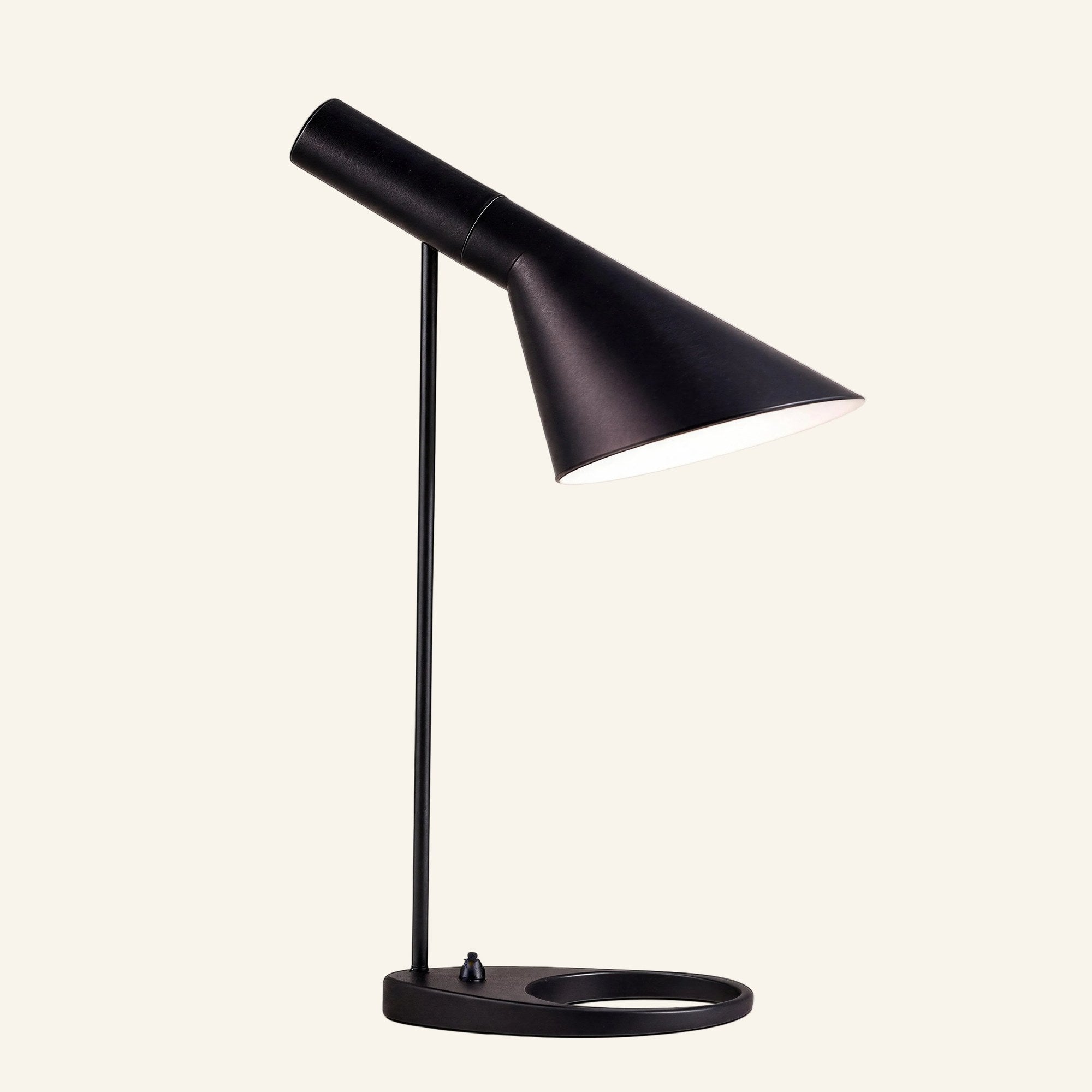 Matte black table lamp with tilting asymmetric cone shade, slim stem and oval ring base, Bauhaus-style metal task light on cream backdrop