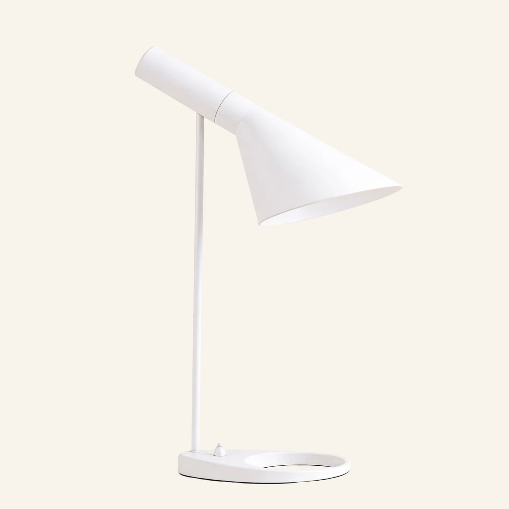 Matte white version of the angled cone table lamp, tilting metal shade on slim stem with oval ring base, shown against soft cream background