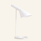 Matte white version of the angled cone table lamp, tilting metal shade on slim stem with oval ring base, shown against soft cream background