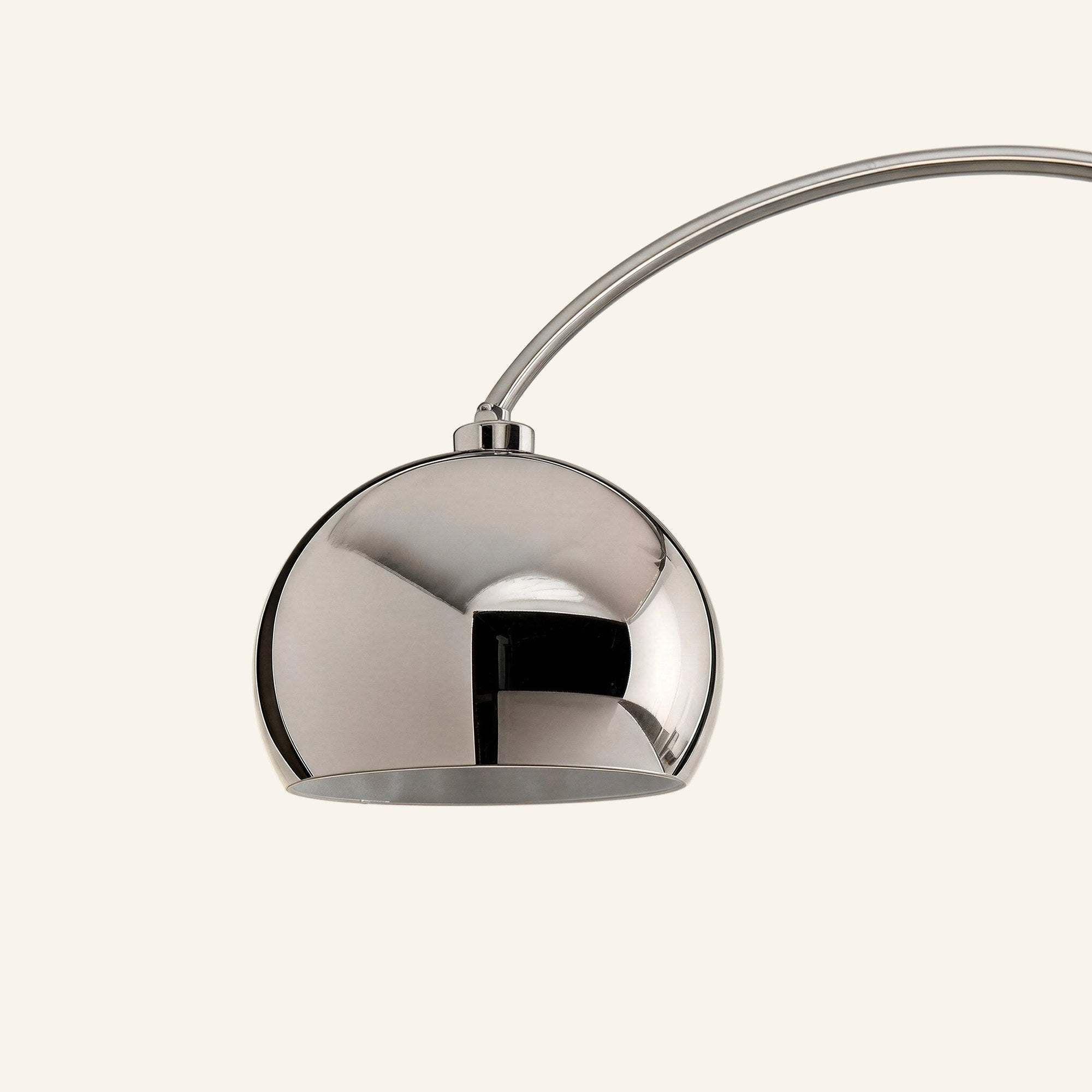 Close-up of the chrome dome shade catching reflections, suspended from a slim arched metal stem against soft neutral background