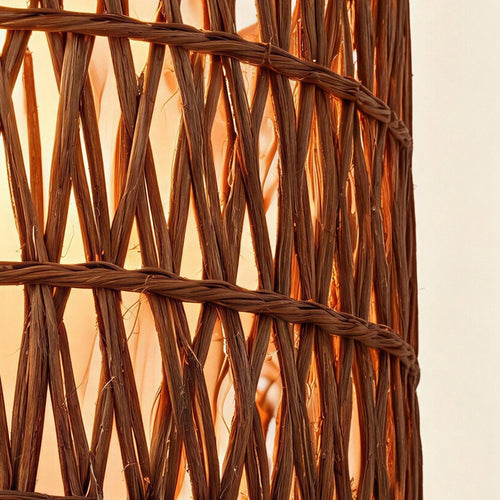 Close-up of the double-woven rattan drum shade showing crosshatched reed strands and warm light glowing through the open weave.
