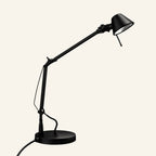 Matte black version of the articulated task lamp showing pivoting joints, cable-tensioned arm, and round weighted base