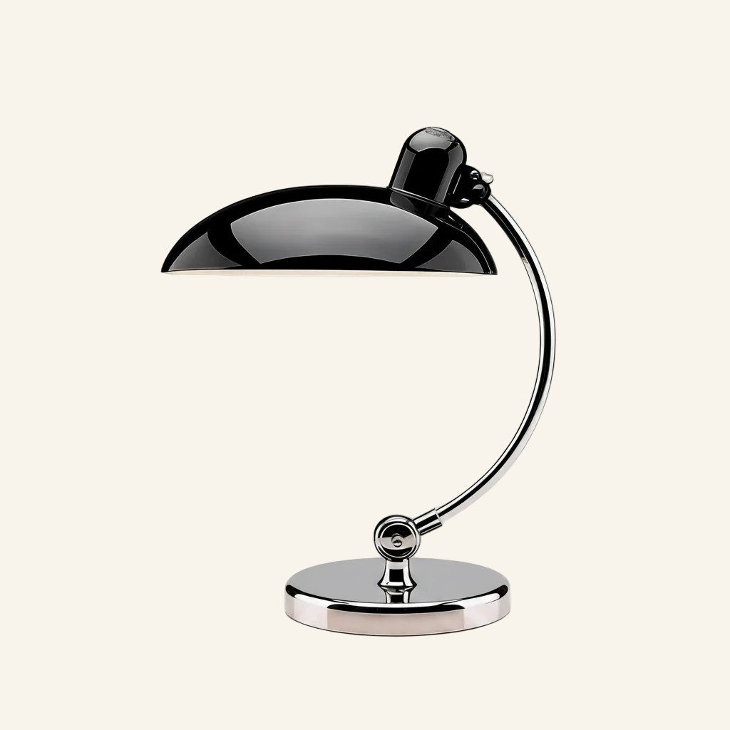 Glossy black domed shade cantilevered from a curved chrome arm on a round polished base, Bauhaus table lamp shown on cream backdrop.