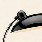 Close-up of the lacquered black dome shade and bulb housing meeting the polished chrome arm, showing reflective metal finish and pivot detail.