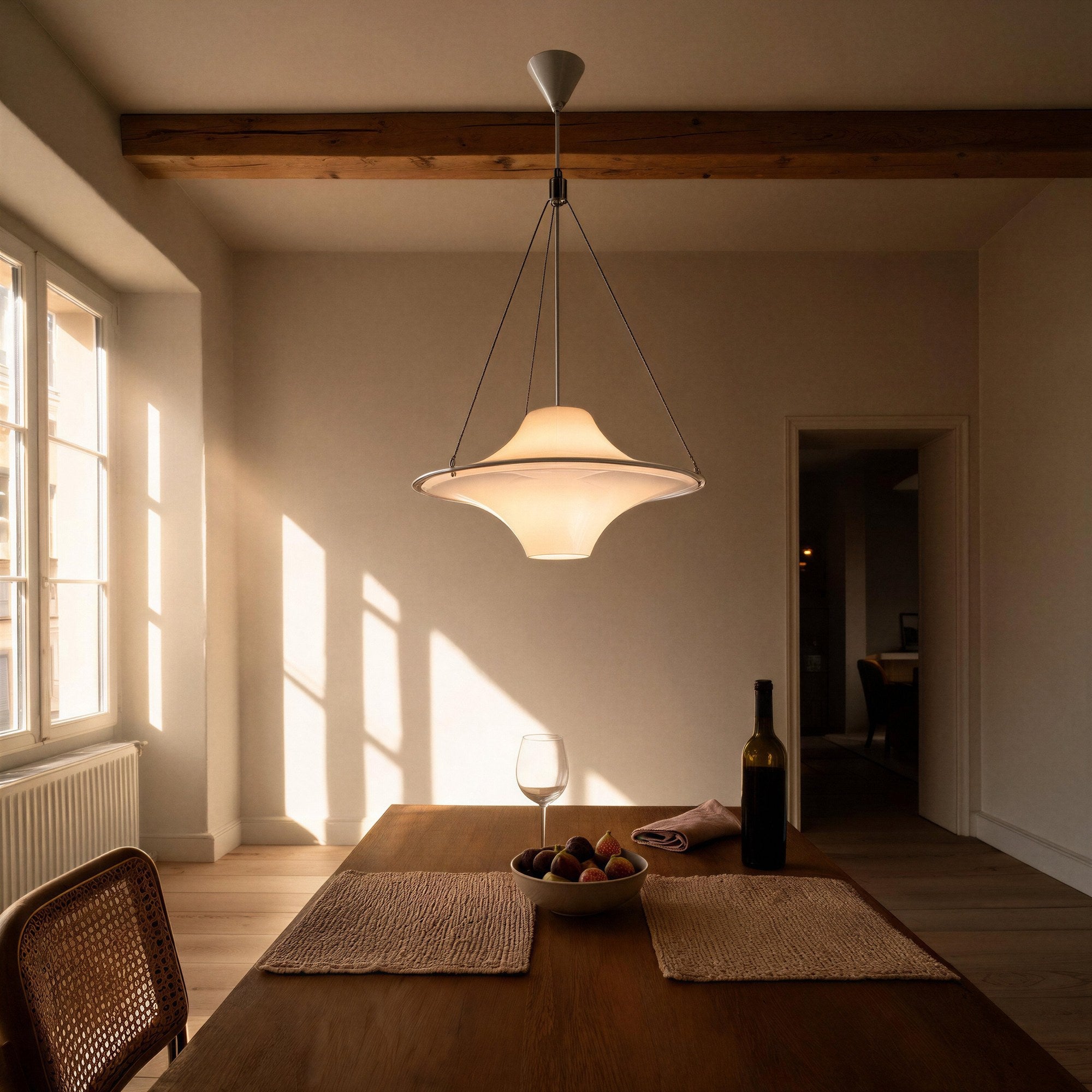 Saucer-shaped glass pendant glows above an oak dining table set with figs and wine, beneath exposed wooden ceiling beams at golden hour