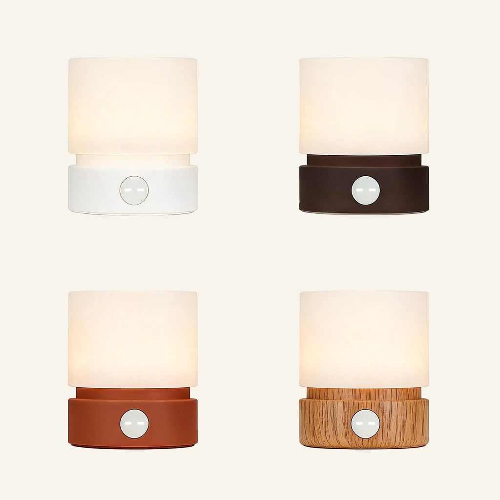 Four colour variants of the cordless mini table lamp arranged in a grid, frosted shades glowing warmly above white, black, terracotta and wood-grain bases