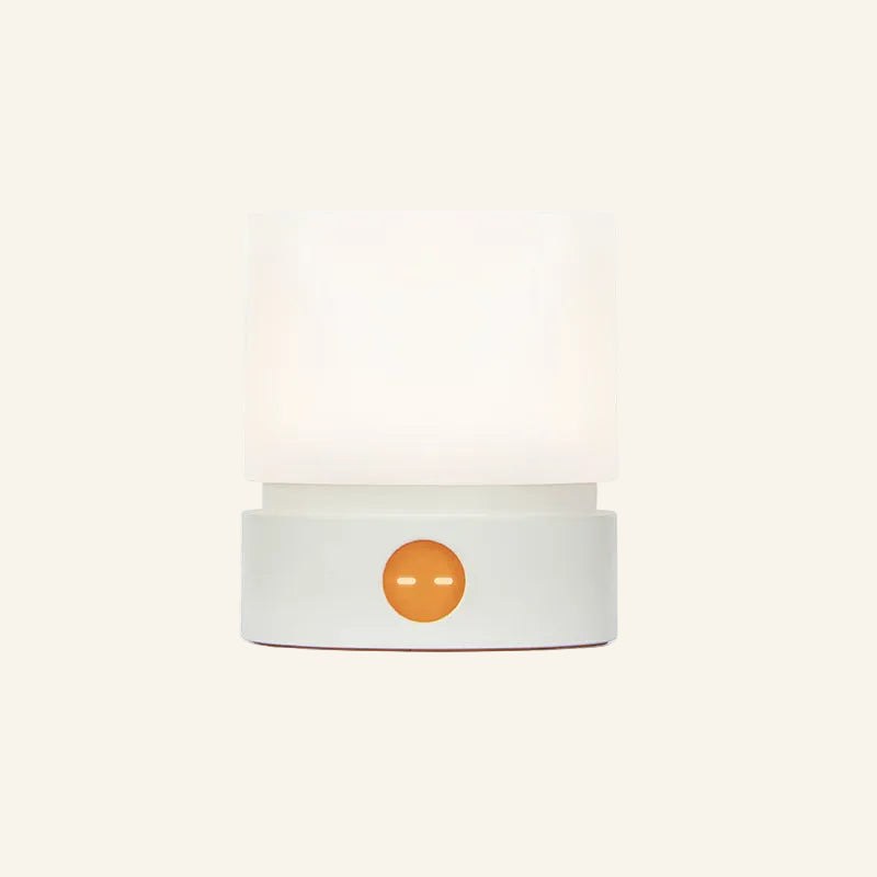 Front view of the cordless LED mini lamp in white, frosted shade lit warmly above a rounded base with glowing amber touch button