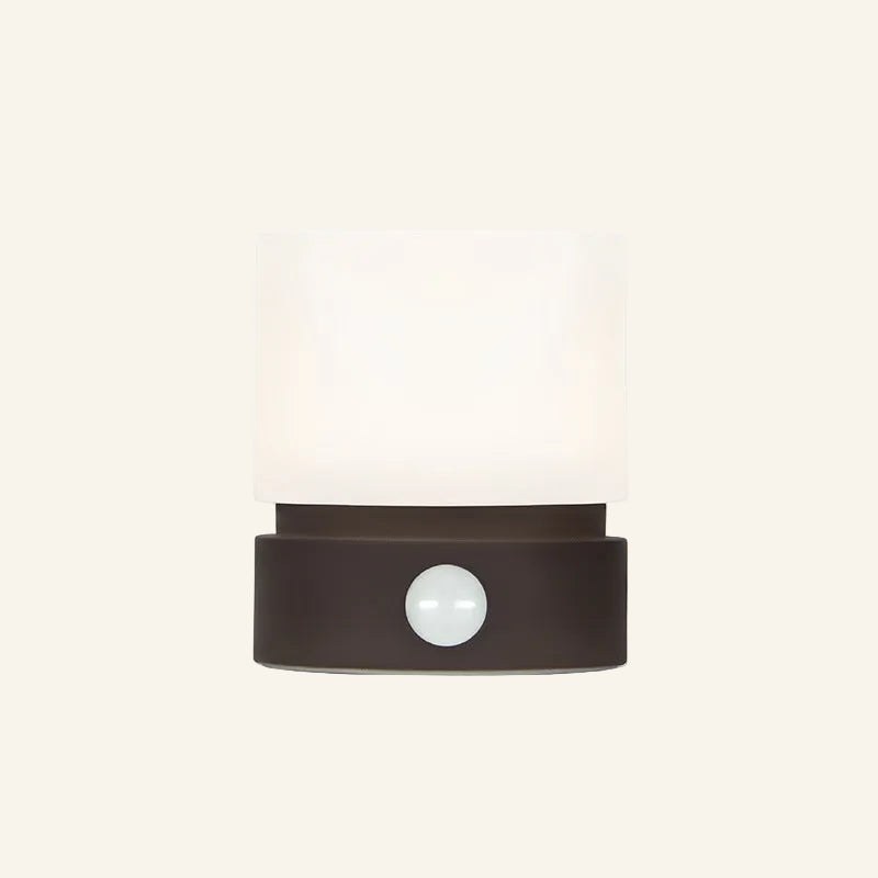 Front view of the rechargeable mini table lamp in dark brown, frosted cylindrical shade resting on a low matte base with central button