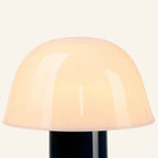 Close-up of the mushroom-shaped opal glass shade showing soft internal glow and glossy surface meeting the deep navy metal stem