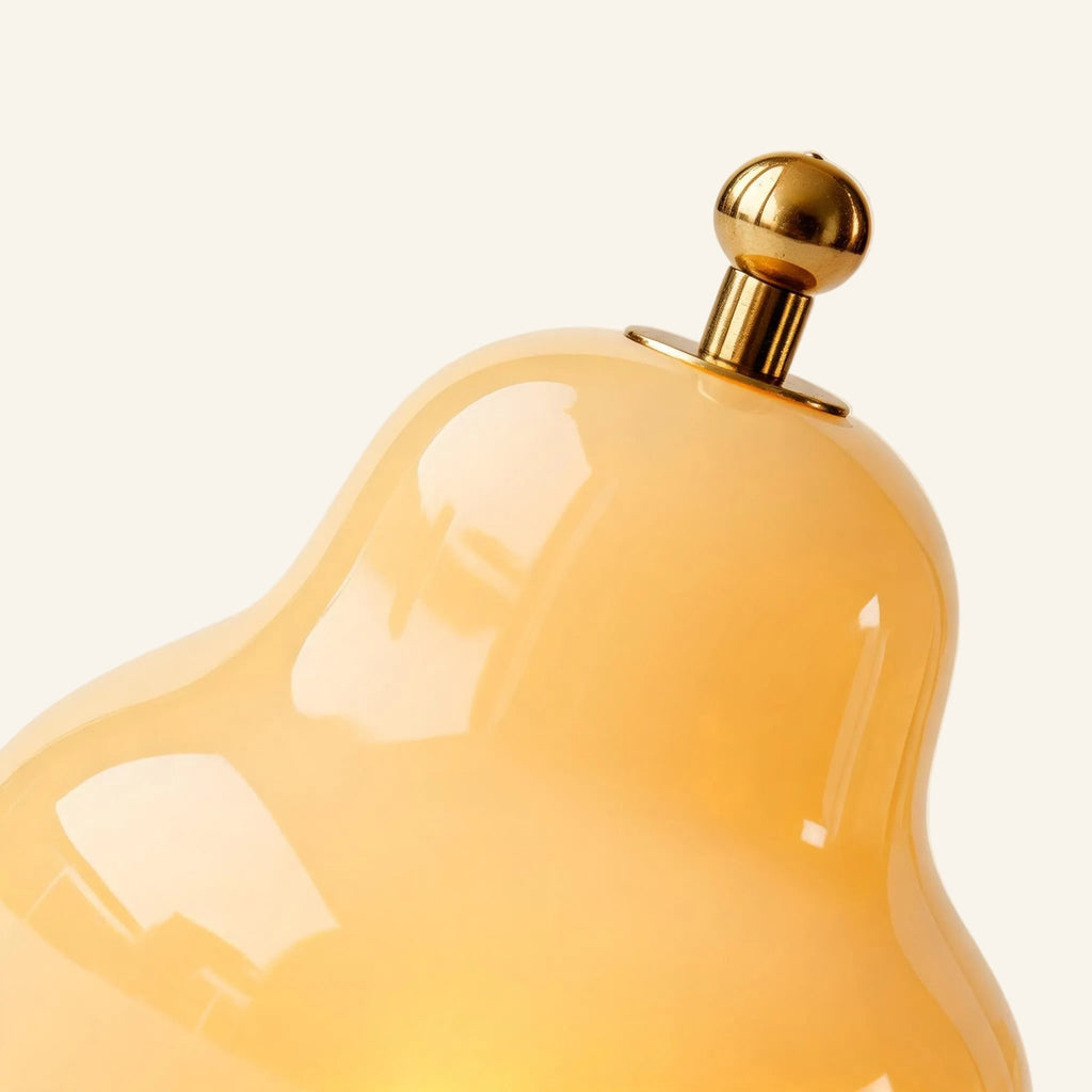 Close-up of the glossy cream glass shade meeting the brass ball finial that doubles as a touch dimmer atop the cordless lamp