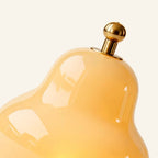 Close-up of the glossy cream glass shade meeting the brass ball finial that doubles as a touch dimmer atop the cordless lamp