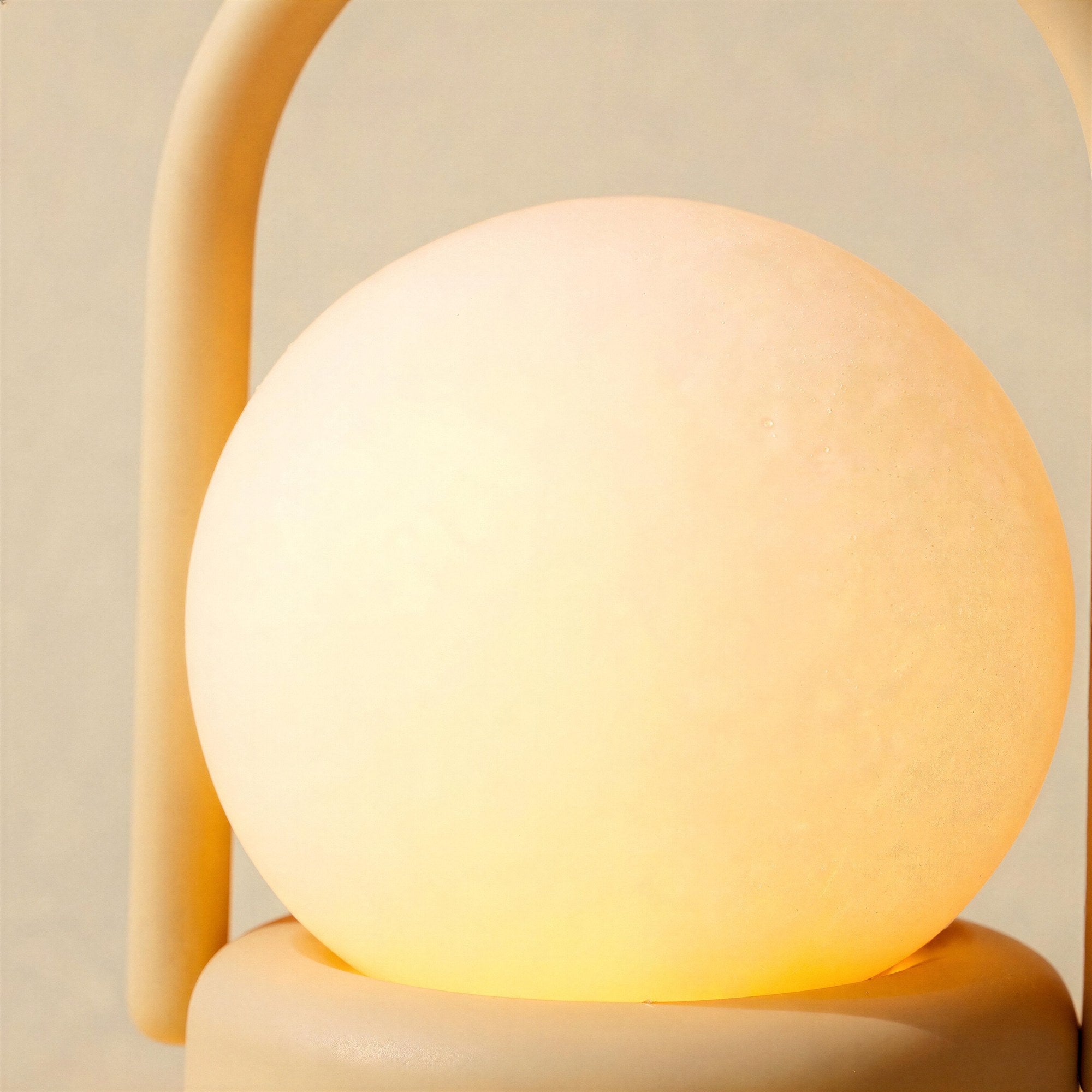 Close-up of the frosted glass globe diffuser resting on its round base, soft matte ABS handle arching behind in warm amber light.