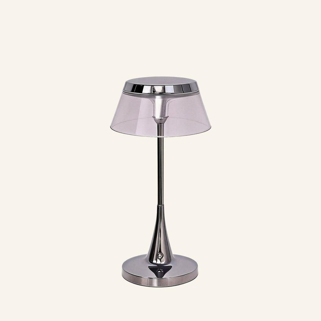 Chrome cordless table lamp with smoked acrylic drum shade and slender tapered stem on a round polished base, studio cream backdrop