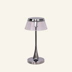 Chrome cordless table lamp with smoked acrylic drum shade and slender tapered stem on a round polished base, studio cream backdrop
