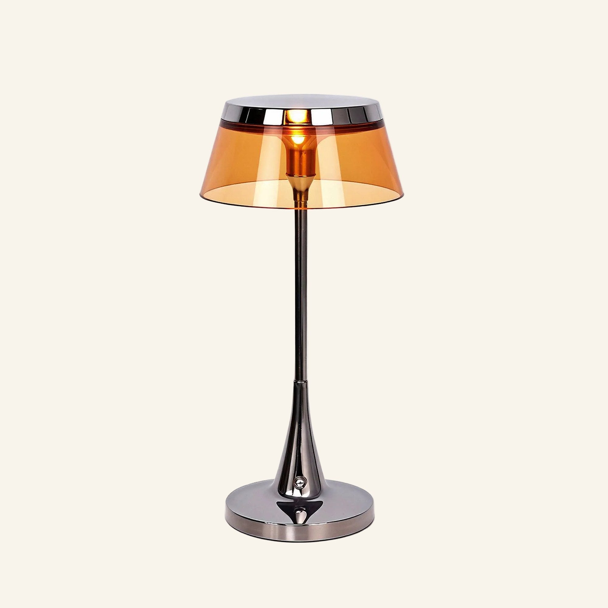 Lamp switched on with warm amber glow filling the tinted acrylic shade, highlighting the chrome stem and weighted disc base