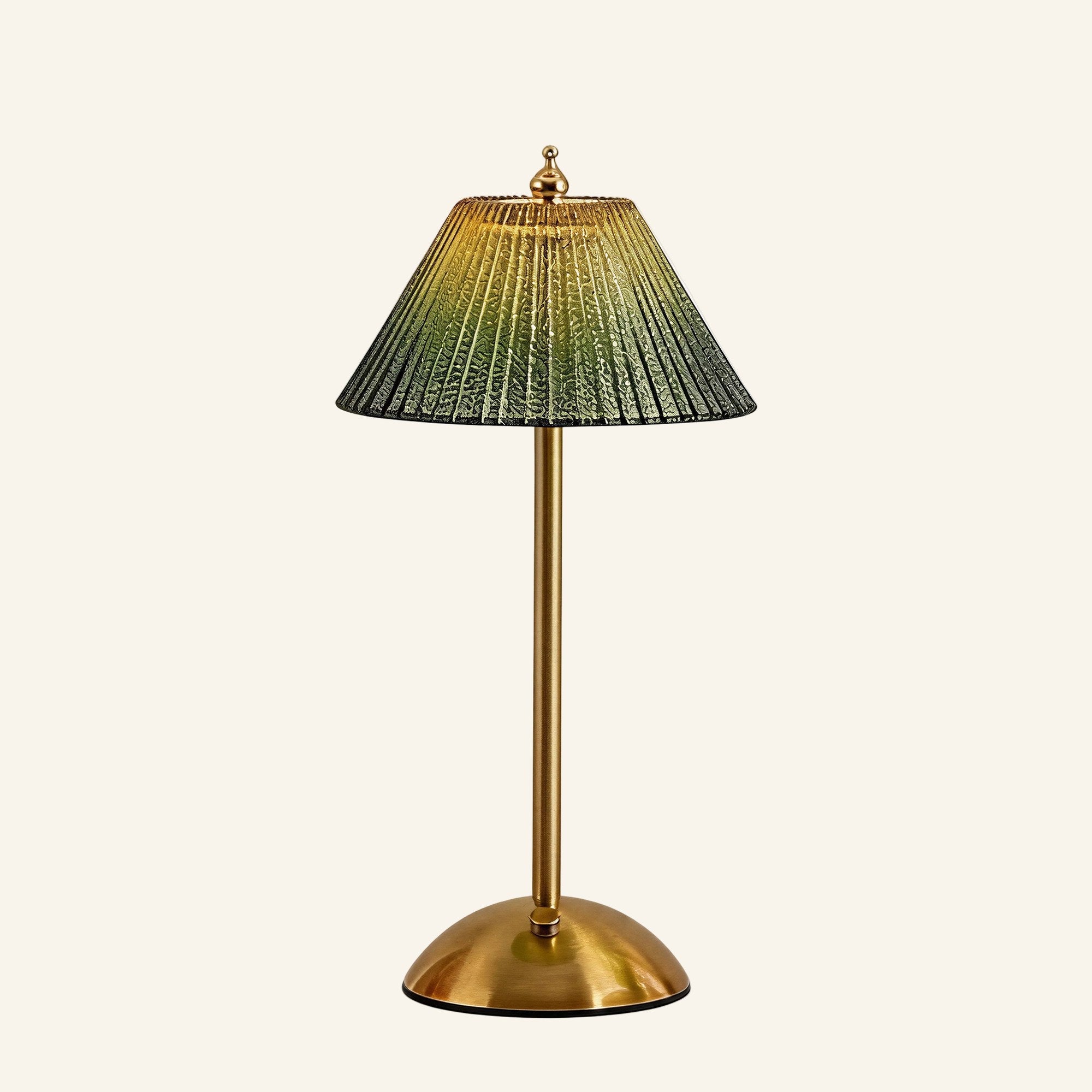 Cordless table lamp with pleated green ribbed-glass shade, brass stem and dome base, illuminated against a cream studio backdrop.