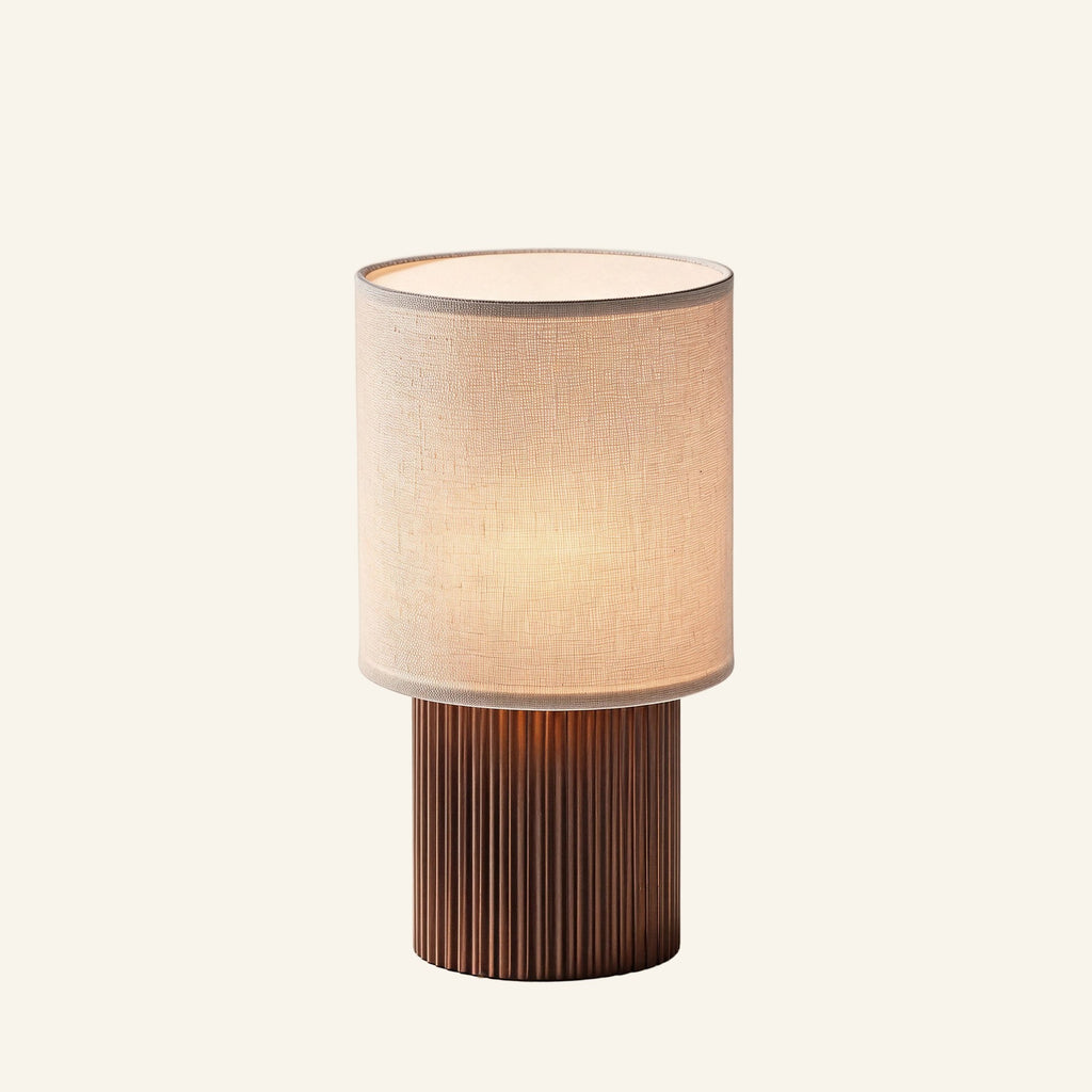 Cordless table lamp with cream linen cylinder shade and fluted copper-brown aluminum base, shown on cream studio background.