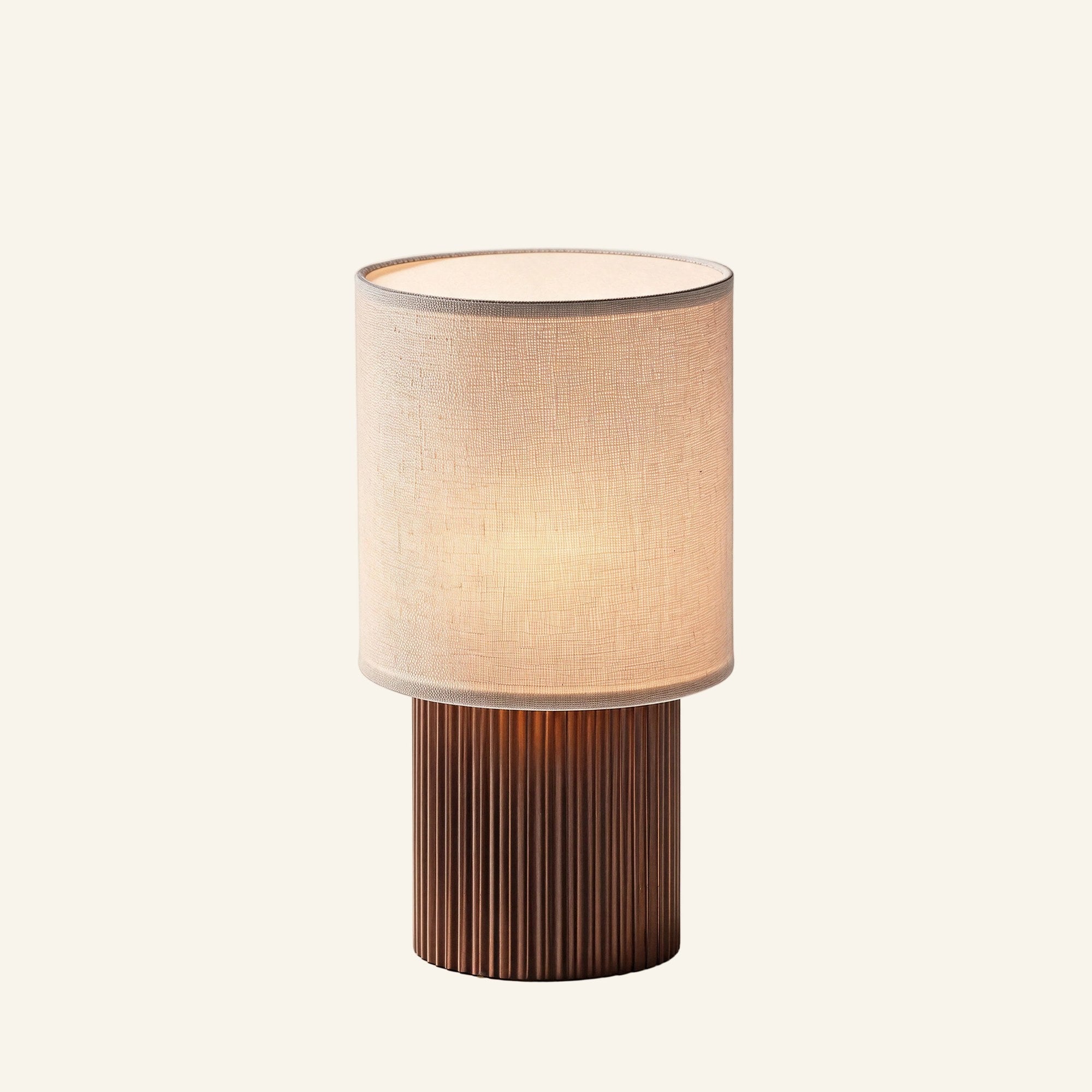 Cordless table lamp with cream linen cylinder shade and fluted copper-brown aluminum base, shown on cream studio background.
