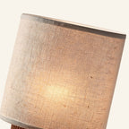 Close-up of woven linen shade revealing natural fiber texture, soft warm glow filtering through the cream cylindrical drum.