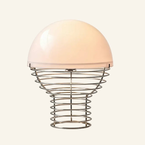 Glossy white glass dome shade resting on a stacked chrome wire cage base, bauhaus table lamp shown on cream studio backdrop.