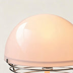 Close-up of the warm-lit opal glass half-sphere shade meeting the polished chrome ring base of a bauhaus table lamp.