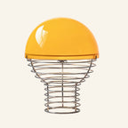 Bright orange glossy glass dome shade atop a concentric chrome wire cage base, retro table lamp colourway shown on cream backdrop.