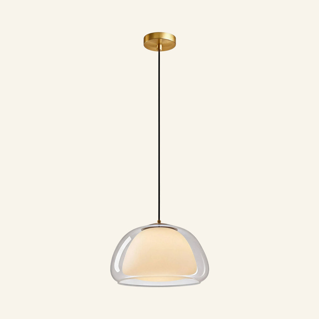 Double glass dome pendant with clear outer shell and opal inner diffuser suspended from brushed brass canopy on cream backdrop