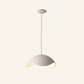 Asymmetric sand-white composite dome pendant on slim drop rod, scooped rim revealing warm LED glow underneath, shown on cream studio backdrop.
