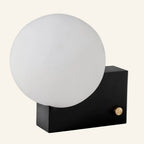 Side angle in black-base finish highlighting the bauhaus contrast between matte cube housing, brass dimmer, and round glass shade.