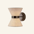 Hourglass wall sconce with two beige linen cones joined by a dark bronze band and round backplate on cream background.