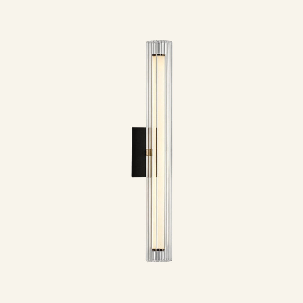 Slim vertical wall sconce with fluted clear glass column, matte black backplate, and brass center band housing a warm LED rod