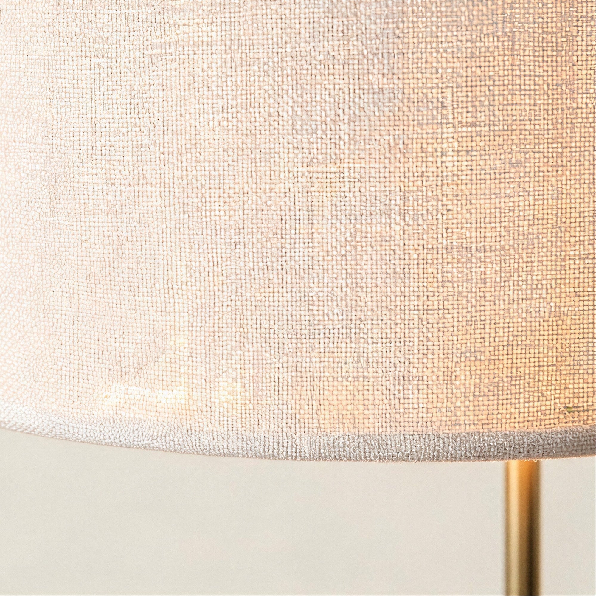 Close-up of the woven white linen drum shade showing textured weave and the gold metal stem rising from below.