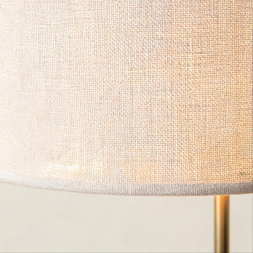 Close-up of the woven white linen drum shade showing textured weave and the gold metal stem rising from below.
