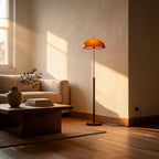 Walnut-stemmed floor lamp casts warm amber light beside a linen sofa and wooden coffee table in a sunlit living room corner