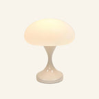 Cordless mushroom table lamp glowing warmly, frosted white dome shade above a glossy ivory tulip base on cream backdrop
