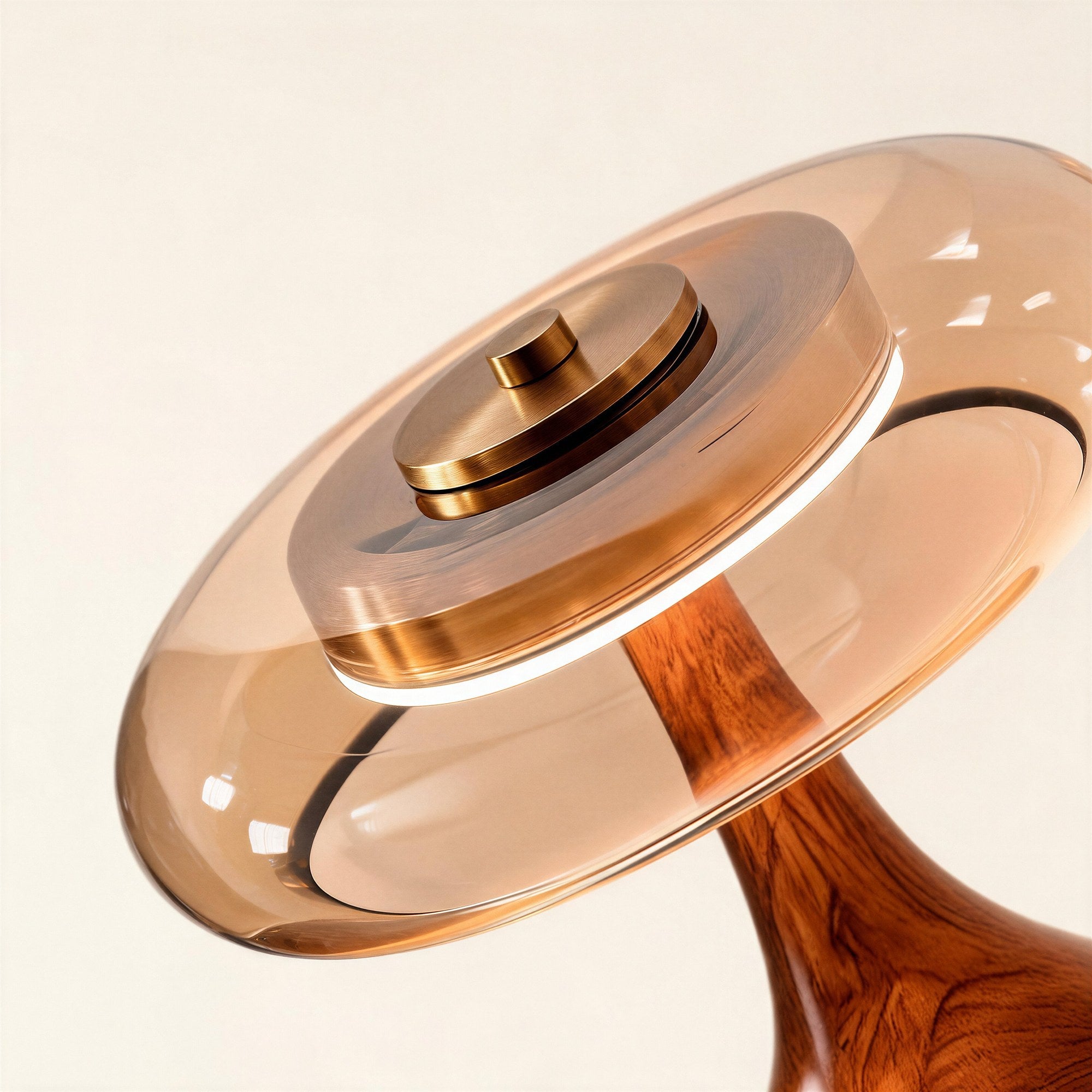 Close-up of the brushed brass top-button switch, amber glass disc shade, and grained walnut neck showing turned-wood and polished metal construction