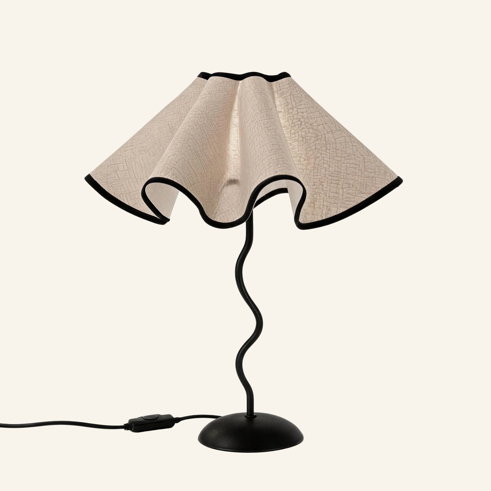 Scalloped linen petal shade with black trim sits atop a wavy black iron stem and domed base, studio shot on cream background.