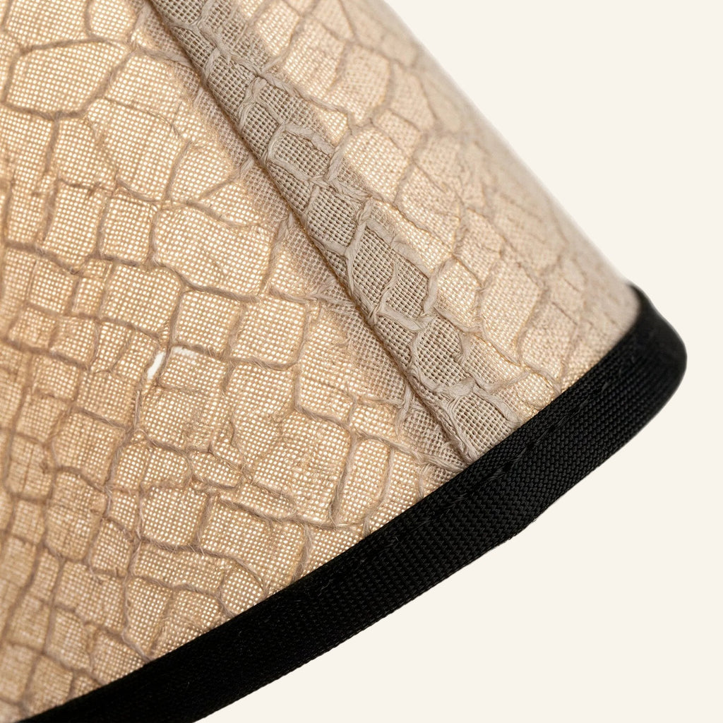 Close-up of the crackle-textured linen-paper shade showing pleated folds and contrasting black fabric trim along the wavy hem.
