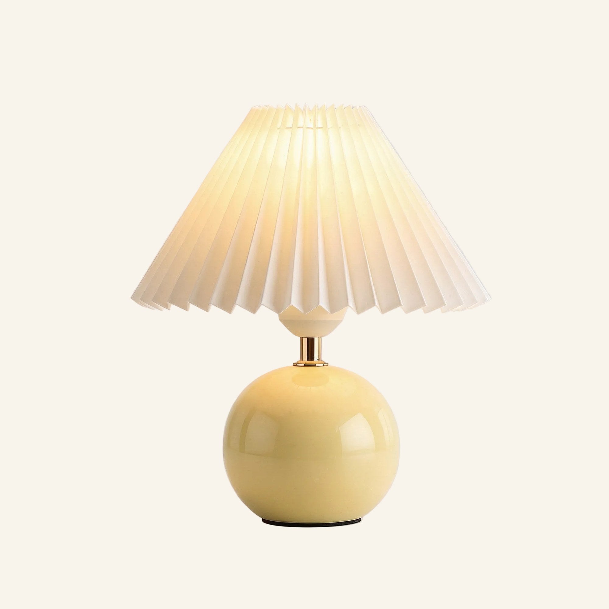 Soft butter-yellow ceramic sphere base supporting a fan-pleated ivory shade, compact bedside lamp shown on neutral background