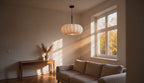 Cinematic video of an off-white pleated pumpkin pendant lamp glowing softly in a sunlit living room with autumn window views.