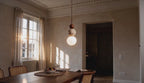Cinematic video of a travertine and wood stacked sphere pendant lamp with frosted opal glass globe glowing above a dining table at sunset.