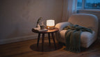 Cinematic evening video of a cordless cylindrical LED mood lamp glowing softly on a wooden side table beside a boucle armchair.