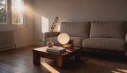 Cinematic video of a frosted glass globe table lamp glowing softly on a wooden coffee table in a sunlit living room.