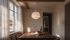 Cinematic video of a layered matte-white acrylic petal pendant lamp glowing above a wooden dining table near sunlit windows.